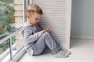 Portrait of a child boy four years old sitting on a wooden floor next to a large window