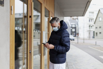 Man wearing face mask using phone in front of entrance door