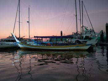 Boats moored in harbor at sunset