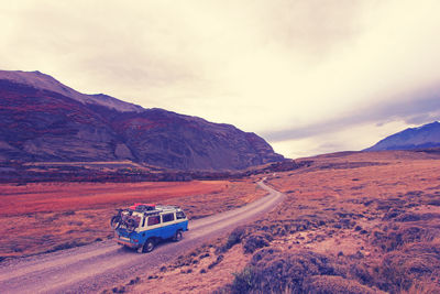 Car on mountain road against cloudy sky