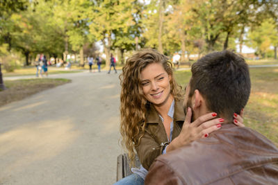 Smiling couple sitting against trees at park