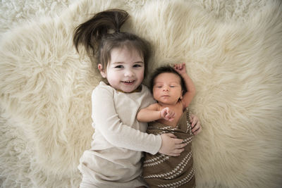 Happy toddler girl snuggles newborn brother, laying on fuzzy white rug