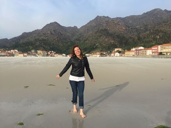 Portrait of smiling young woman standing on beach against sky