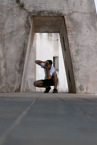 Full length of young man sitting against wall in building