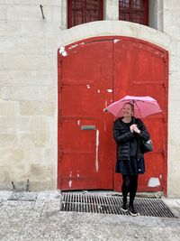 Rear view of woman with umbrella standing against wall