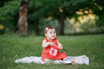 Adorable cute little caucasian baby toddler girl in red dress waving canadian flag in park outdoors. 