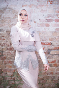 Portrait of young woman standing against brick wall