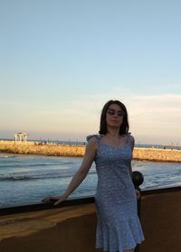 Portrait of young woman standing against sea against sky