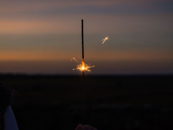 Silhouette hand holding sparkler against sky during sunset