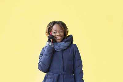 Portrait of smiling young woman talking on phone against yellow background