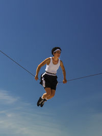 Low angle view of young woman jumping against clear sky