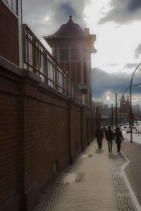 People walking on road against cloudy sky