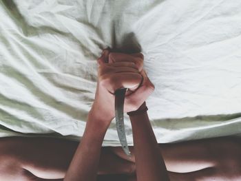 Low section of woman holding knife while sitting on bed at home
