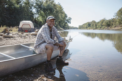 Portrait of smiling man sitting on boat at lakeshore