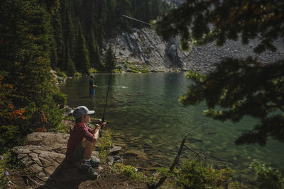 Father and son fishing in lake against mountains at forest