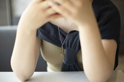 Girl sitting at table. elbows on table. people waiting. hands raised.