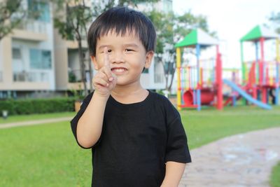 The little asian boy pointing his right hand up on the playground.