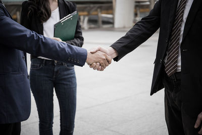 Midsection of businessmen shaking hands with businesswoman in city