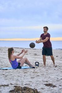 Friends exercising with ball at beach against sky