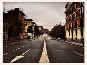 Road passing through city against cloudy sky