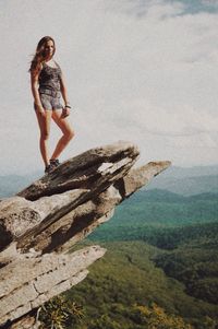 Hiker standing on rock formation against cloudy sky