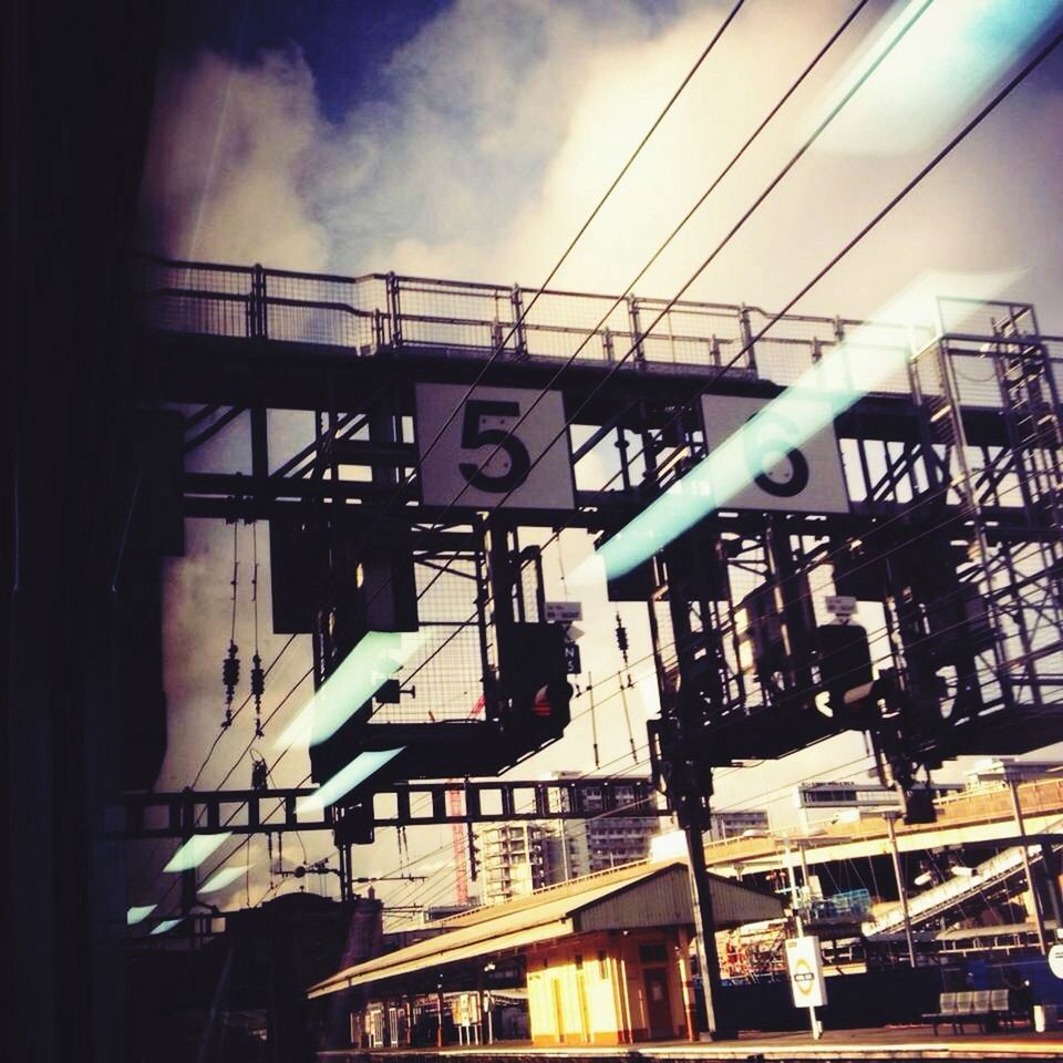 sky, built structure, low angle view, architecture, transportation, text, public transportation, communication, cloud - sky, western script, building exterior, mode of transport, railroad station, day, transfer print, cloudy, auto post production filter, indoors, cloud, rail transportation