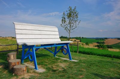 Empty bench on field against sky