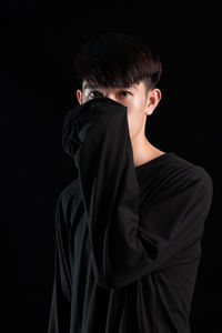 Side view of young woman standing against black background