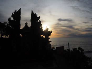 Silhouette built structure by sea against sky during sunset