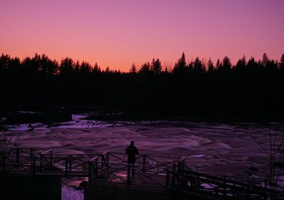 Silhouette trees by lake against sky during sunset