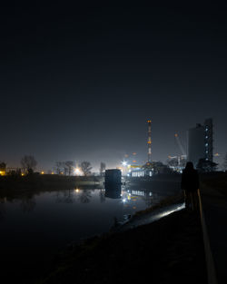 Illuminated factory by river against sky at night