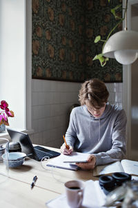 Serious teenage boy writing on book while doing homework