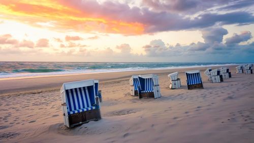 Hooded chairs on beach against sky during sunset