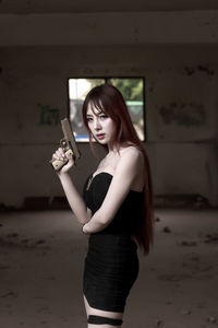Portrait of young woman holding handgun against wall