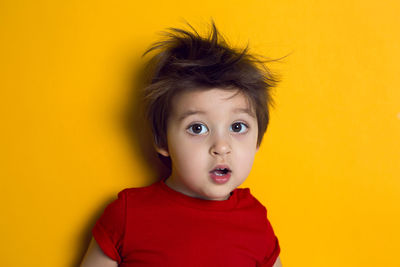 Cheerful baby boy in red t-shirt stands on yellow background