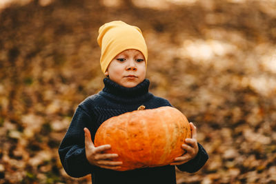 Happy funny little boy teen child in a hat holding a big pumpkin is getting ready for halloween