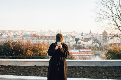 Woman standing by tree in city against sky during winter