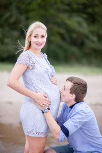 Man crouching while kissing stomach of pregnant wife at beach