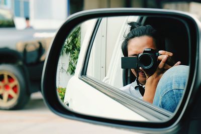Reflection of man photographing on side-view mirror of car