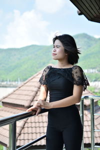 Young woman looking away while standing by railing against clear sky in balcony