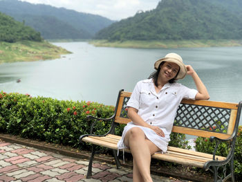 Portrait of woman sitting on bench against river