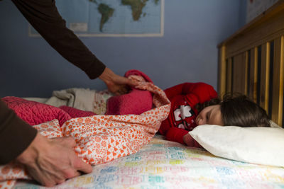 Cropped hands of father covering blanket on sleeping daughter in bedroom