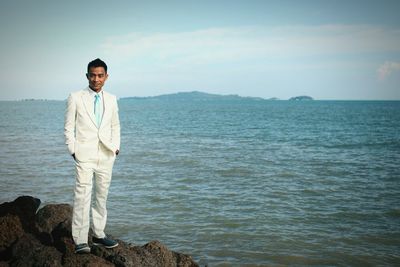 Portrait of well-dressed young man standing on rock by sea