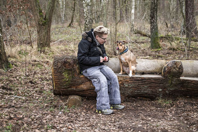 Rear view of woman with dog sitting on tree trunk in forest