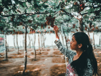 Side view of young woman standing against trees