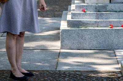 The legs of a woman in a grey dress in an uncertain pose near a memorial