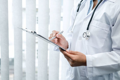 Midsection of doctor writing in clipboard at hospital