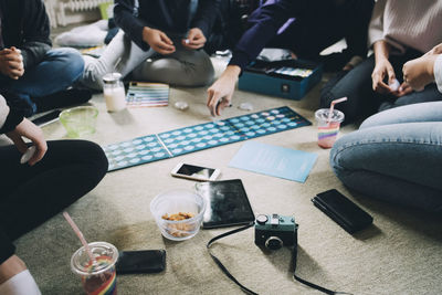 Low section of friends playing board games while having snacks on floor at home