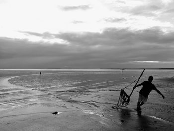 Man pulling fishing equipment on shore at beach