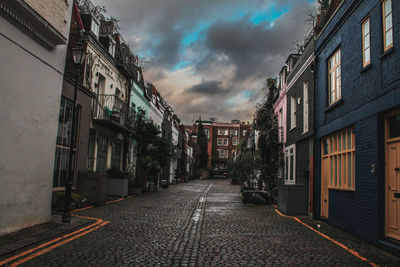 Narrow street amidst buildings against cloudy sky